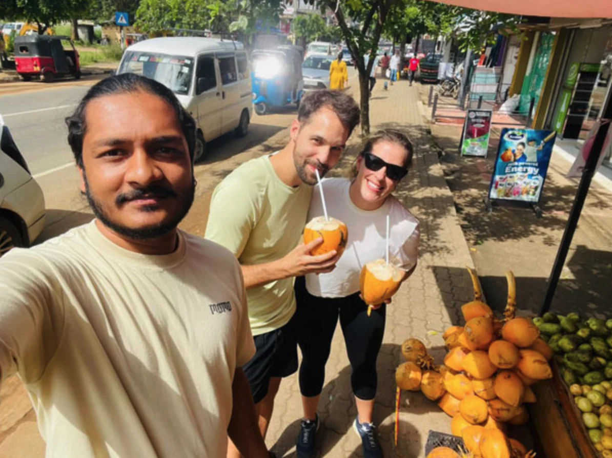 Traveling couple enjoying a roadside coconut stop with their Sri Lankan driver